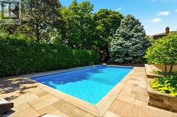 Rectangular in-ground swimming pool with an integrated ladder, surrounded by stone paver decking -