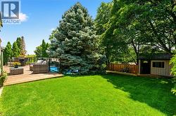 Expansive lawn with a wood-finish deck, glass panel railing, and a visible pool -