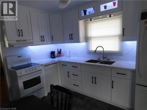 White shaker-style cabinetry with matte black hardware, dual basin stainless steel sink, under-cabinet lighting, white countertop, and backsplash with subtle veining - 625 Tate Avenue, Hamilton, ON 