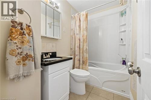White vanity with a dark countertop, white toilet, and a white bathtub with integrated shelving - 625 Tate Avenue, Hamilton, ON 