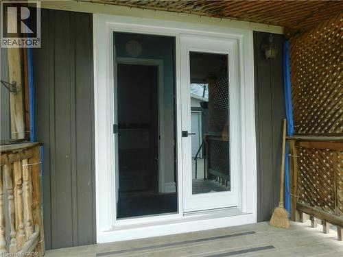New White-framed FRENCH glass doors, dark vertical panel siding, exterior wall-mounted light fixture, and wooden deck railing - 625 Tate Avenue, Hamilton, ON 