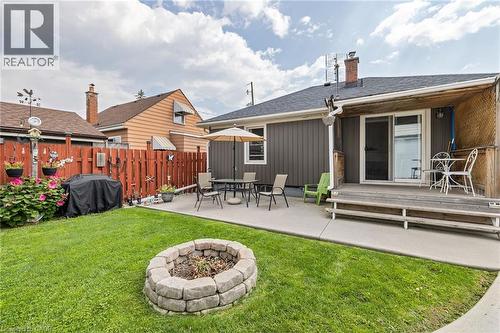 Expansive backyard featuring a manicured lawn, stone fire pit, concrete patio, and a wood deck with sliding glass door access - 625 Tate Avenue, Hamilton, ON 