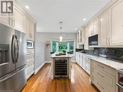 Gourmet kitchen featuring stainless steel appliances, extensive cabinetry, light-toned countertops, a central island with integrated wine refrigeration, and rich wood-finish flooring - 