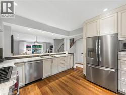 Kitchen featuring wood-finish flooring, light-toned cabinetry, stainless steel appliances, and stone countertops - 