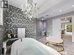 Freestanding soaking tub with floor-mounted faucet, crystal chandelier, glass-enclosed shower, patterned accent wall, and recessed ceiling lighting - 