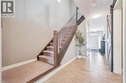 Foyer featuring wood-finish tile flooring, a carpeted staircase with wood handrails, and a modern barn door - 