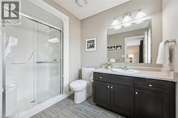 Shower with clear glass enclosure, dark wood-finish vanity with white countertop, integrated sink, large wall-mounted mirror, and decorative overhead lighting - 