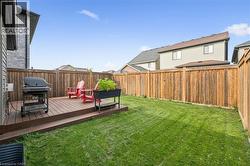 Spacious backyard oasis featuring a manicured lawn, composite deck with integrated seating area, gas grill, mature landscaping with planters, and wood privacy fencing - 
