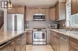 Wood-finish cabinetry with stainless steel hardware, stainless steel appliances, stone countertops, hexagonal tile backsplash, and a stainless steel kitchen sink - 