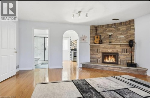 Corner stone-clad fireplace with hearth, wood-finish flooring, and white interior doors - 85 Summerlea Drive, Hamilton, ON 