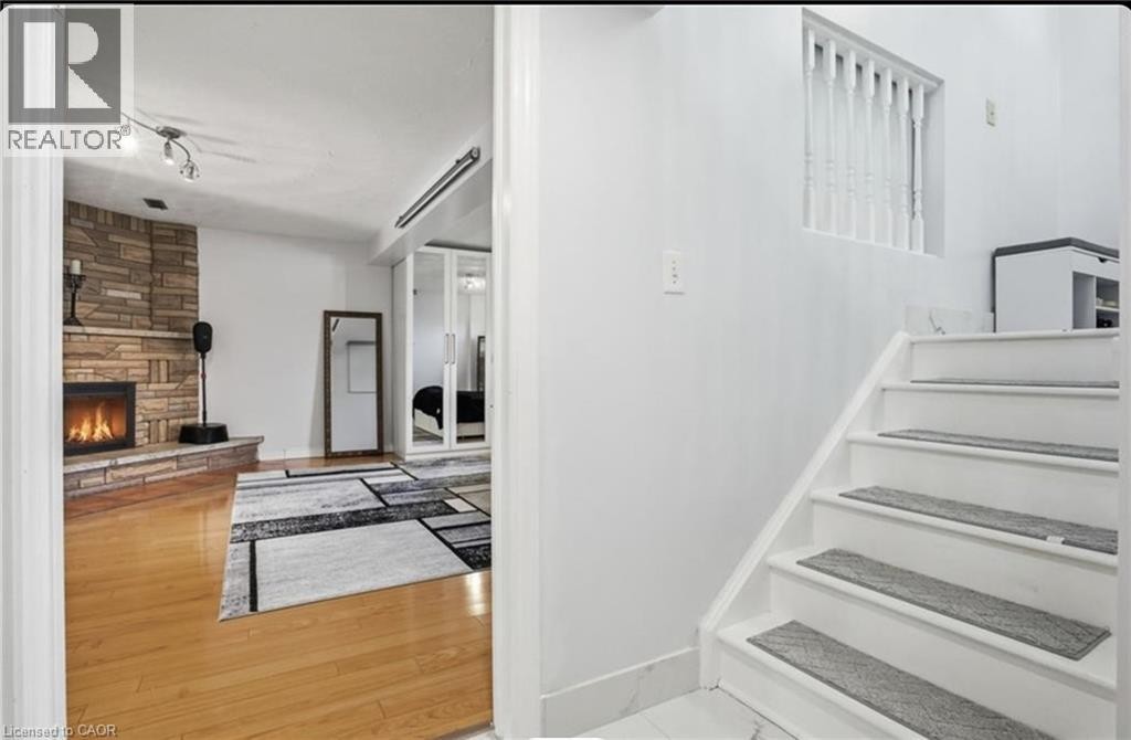 Stone-clad fireplace feature with a raised hearth, wood-finish flooring, white painted staircase, and white baluster railing - 85 Summerlea Drive, Hamilton, ON