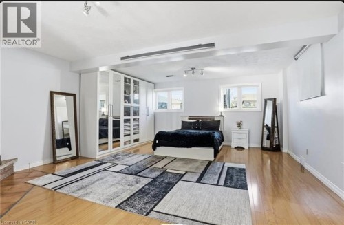 Expansive room featuring wood-finish flooring, two windows, and built-in closet units with mirrored doors - 85 Summerlea Drive, Hamilton, ON 