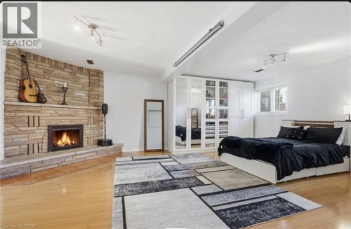 Hardwood flooring, stone-clad corner fireplace, built-in white cabinetry, integrated track lighting, and a multi-pane window - 85 Summerlea Drive, Hamilton, ON 