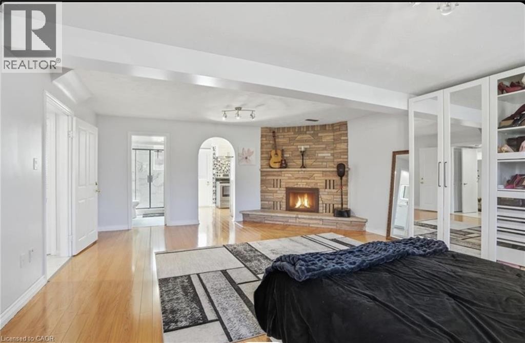 Stone-clad fireplace with a hearth, light wood-finish flooring, built-in mirrored wardrobes, and an arched doorway - 85 Summerlea Drive, Hamilton, ON