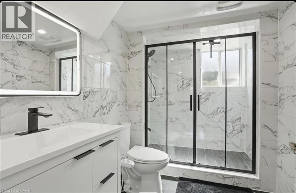 Marble-look tile walls, modern vanity with integrated sink, black-framed glass shower enclosure, matte black fixtures, and an illuminated mirror - 85 Summerlea Drive, Hamilton, ON