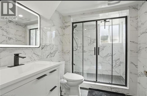 Marble-look tile walls, modern vanity with integrated sink, black-framed glass shower enclosure, matte black fixtures, and an illuminated mirror - 85 Summerlea Drive, Hamilton, ON 