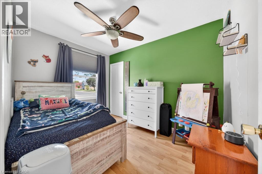 Hardwood-finish flooring, ceiling fan with integrated lighting, window with blinds and drapes, and a brightly painted accent wall - 420 Upper Gage Avenue, Hamilton, ON