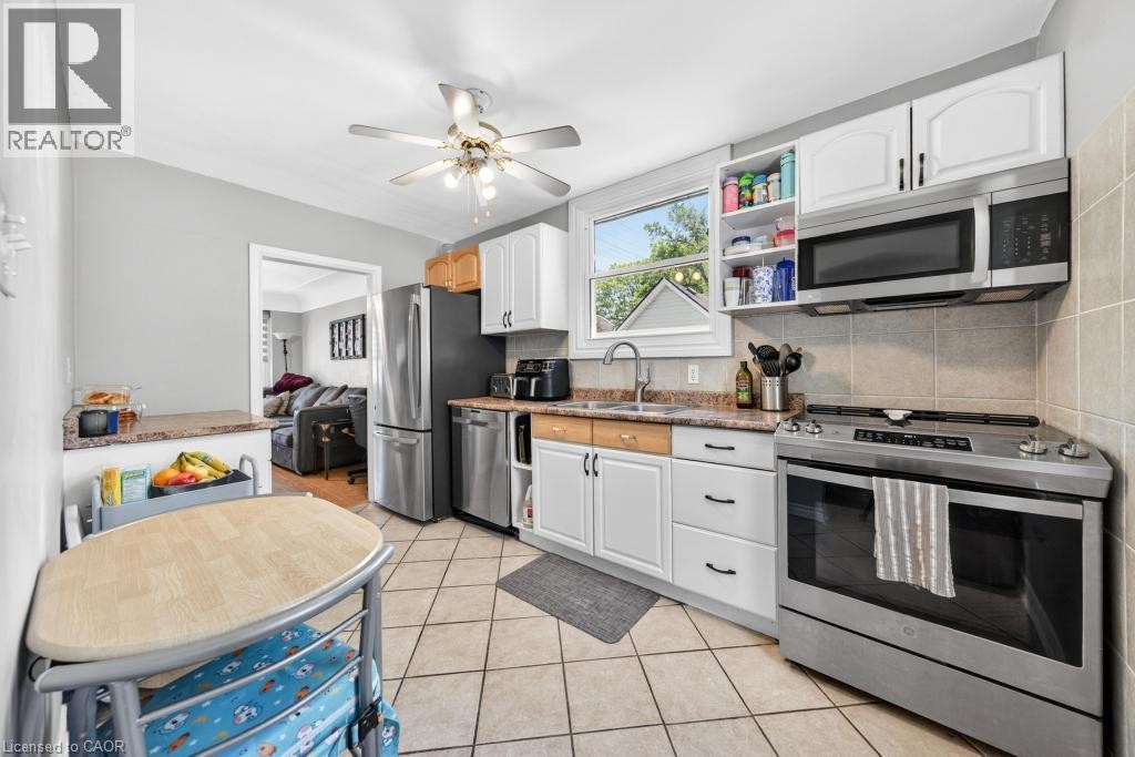 Kitchen featuring white cabinetry, stainless steel appliances, a ceiling fan, a window, and tile flooring - 420 Upper Gage Avenue, Hamilton, ON