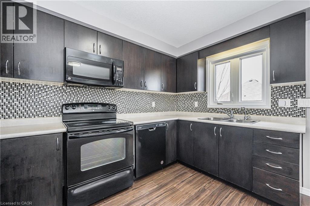 Kitchen featuring dark wood-finish cabinetry, black appliances, a mosaic tile backsplash, and light countertops - 224 Jessica Crescent Unit# B, Kitchener, ON