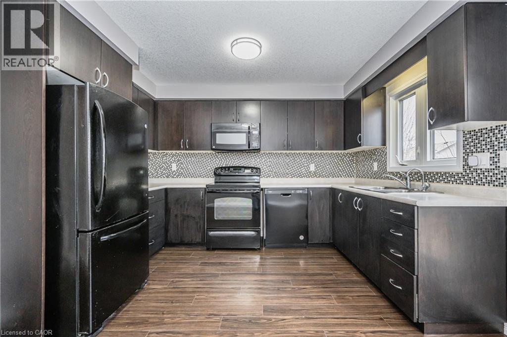 Kitchen featuring dark wood-finish cabinetry, white countertops, a mosaic tile backsplash, wood-finish flooring, and black appliances - 224 Jessica Crescent Unit# B, Kitchener, ON