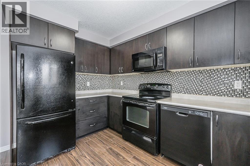 Dark wood-finish cabinetry, black appliances, mosaic tile backsplash, light countertops, and wood-finish flooring - 224 Jessica Crescent Unit# B, Kitchener, ON