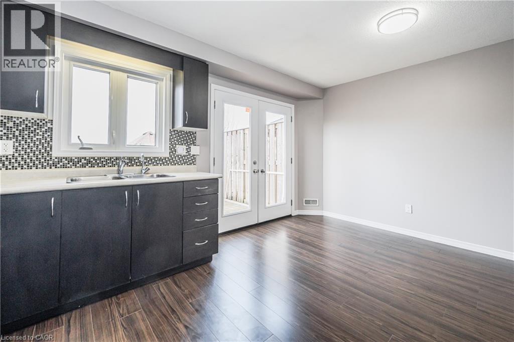 Dark wood-finish flooring, two-tone kitchen cabinetry, mosaic tile backsplash, double patio doors with frosted glass, and a large window above the sink - 224 Jessica Crescent Unit# B, Kitchener, ON