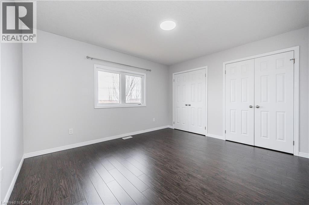 Dark wood-finish flooring, white walls, two windows, two sets of white bi-fold doors, and recessed ceiling lighting - 224 Jessica Crescent Unit# B, Kitchener, ON
