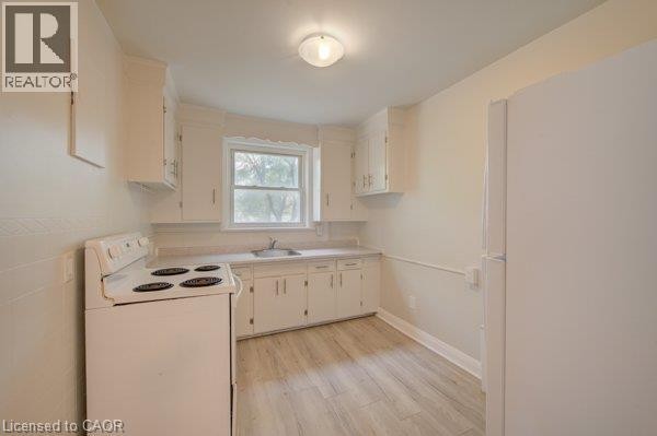 Kitchen featuring wood-finish flooring, white cabinetry, a single basin sink, a window, and a ceiling-mounted light fixture - 141 Chapel Street, Kitchener, ON