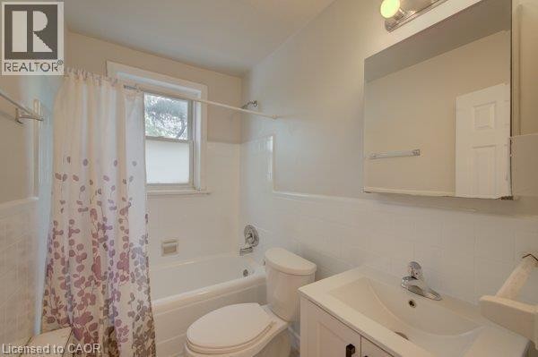 White ceramic tile walls, built-in bathtub with shower fixture, single-pane window, white vanity with integrated sink, and wall-mounted mirror - 141 Chapel Street, Kitchener, ON