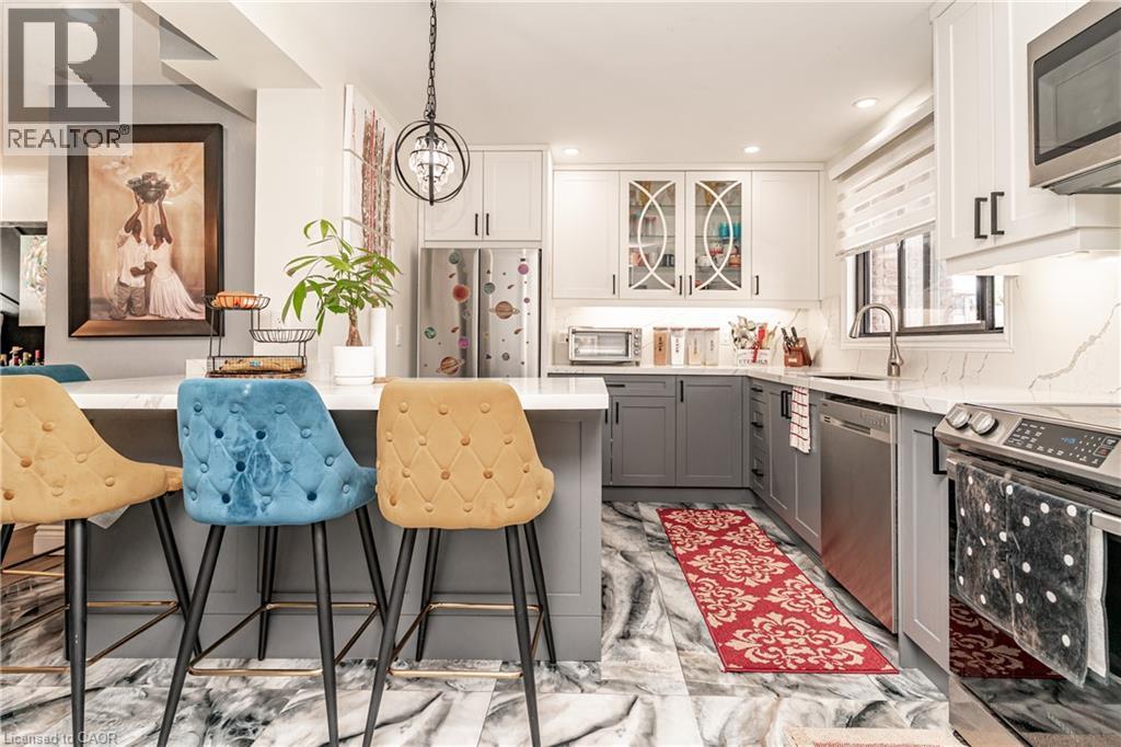 Contemporary kitchen featuring a large island with a solid surface countertop, stainless steel appliances, two-tone cabinetry, and a spherical pendant light fixture - 52 Charters Road, Brampton, ON
