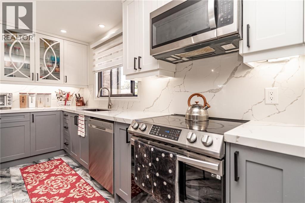 White cabinetry, gray lower cabinetry, stainless steel appliances, patterned backsplash, and under-cabinet lighting - 52 Charters Road, Brampton, ON