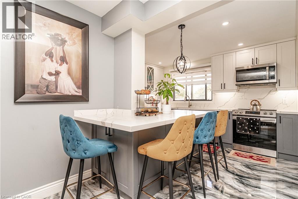 Kitchen featuring a peninsula with a light-toned countertop, stainless steel appliances, upper and lower cabinetry, and recessed lighting - 52 Charters Road, Brampton, ON