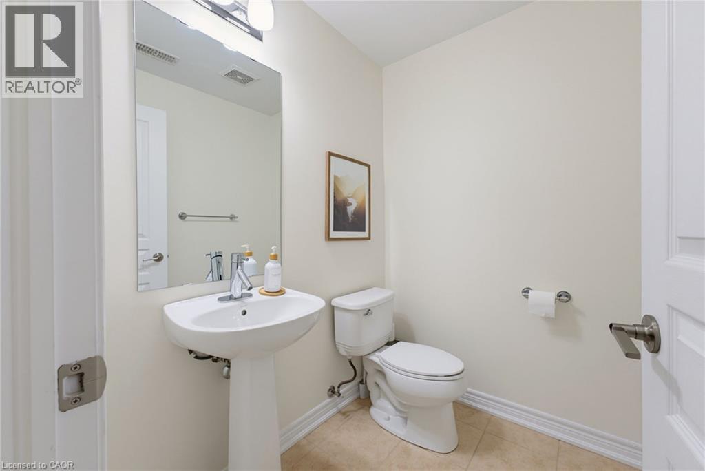 Pedestal sink with chrome-finish faucet, ceramic toilet, wall-mounted mirror, and tile flooring - 541 Winston Road Unit# 50, Grimsby, ON