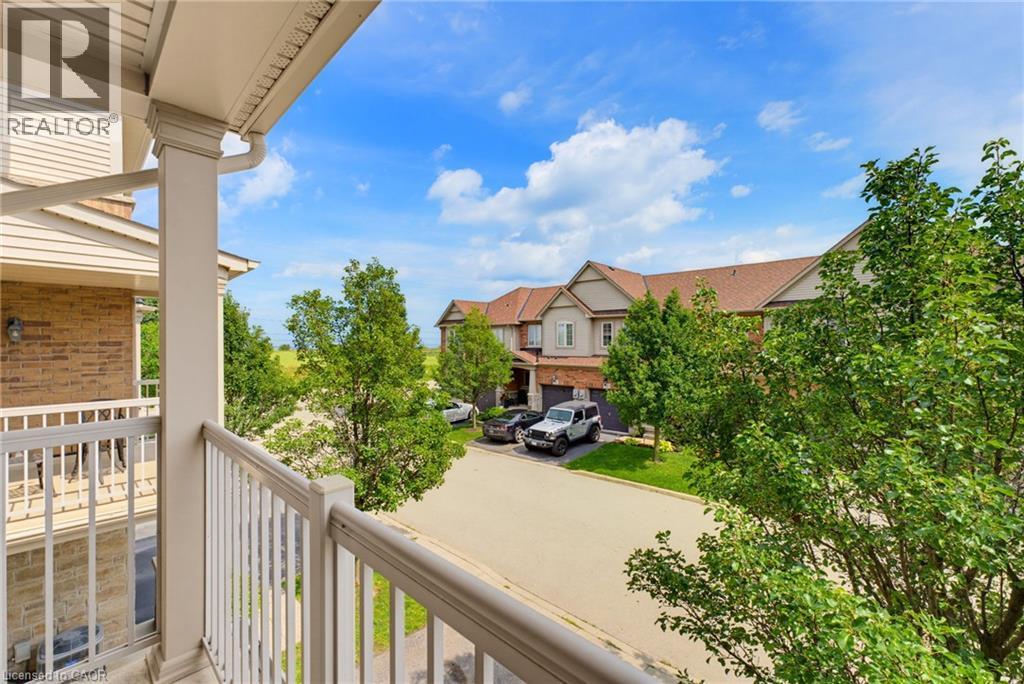 Balcony with white railings, brick and siding exterior, green trees, and paved street - 541 Winston Road Unit# 50, Grimsby, ON