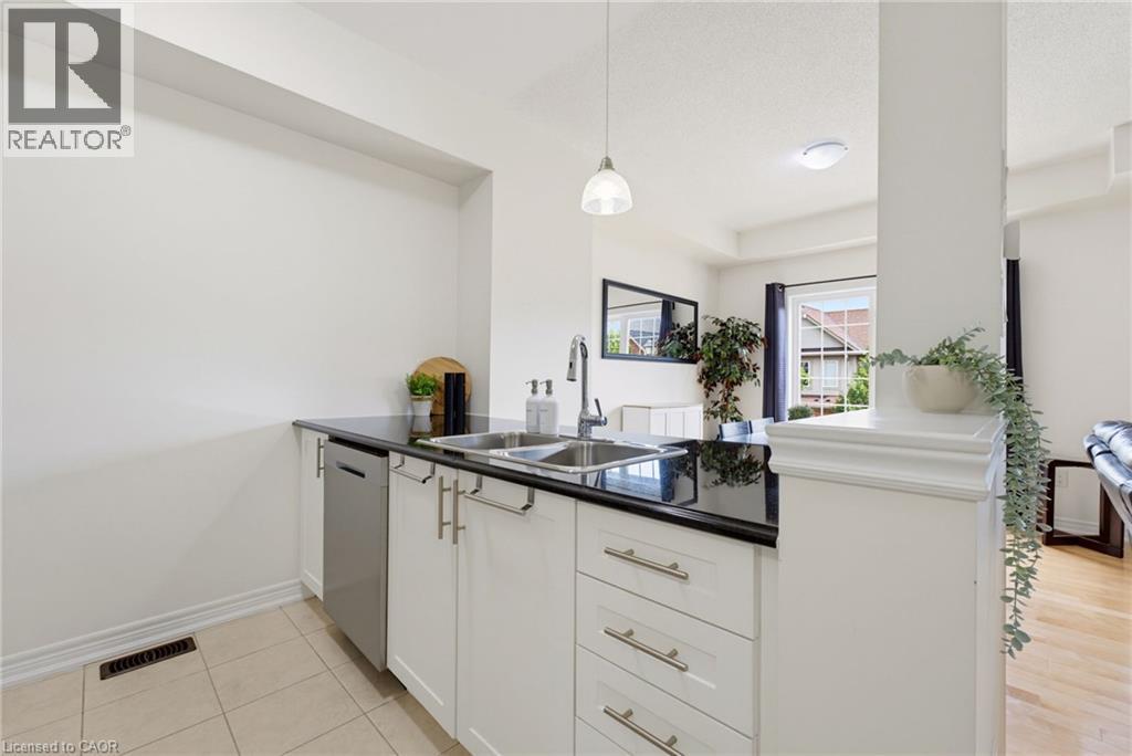White cabinetry with brushed nickel hardware, black countertop, stainless steel double basin sink, and integrated dishwasher - 541 Winston Road Unit# 50, Grimsby, ON