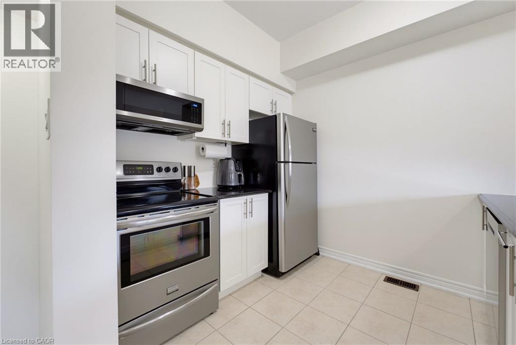 Kitchen with white cabinetry, stainless steel appliances, dark countertops, and light-toned tile flooring - 541 Winston Road Unit# 50, Grimsby, ON
