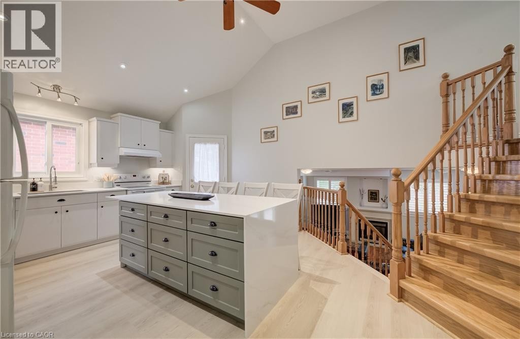 Vaulted ceiling with a ceiling fan, light wood-finish flooring, white cabinetry, a kitchen island with gray drawers, and a wood staircase - 245 Fern Crescent, Waterloo, ON