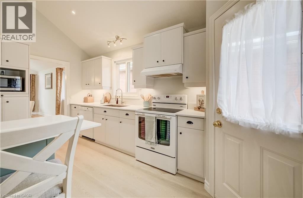 Kitchen featuring white cabinetry, light-toned wood-finish flooring, white appliances, and a vaulted ceiling - 245 Fern Crescent, Waterloo, ON