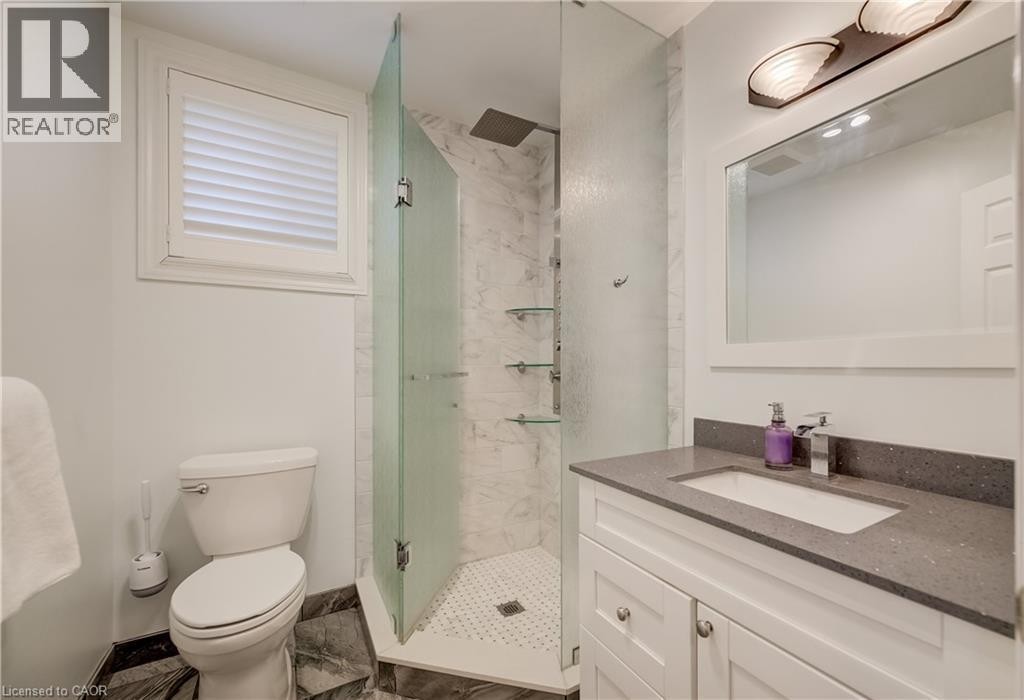 Bathroom featuring a glass-enclosed shower with a rain showerhead, a white vanity with a gray countertop, a rectangular sink, and a white framed mirror with an overhead light fixture - 245 Fern Crescent, Waterloo, ON