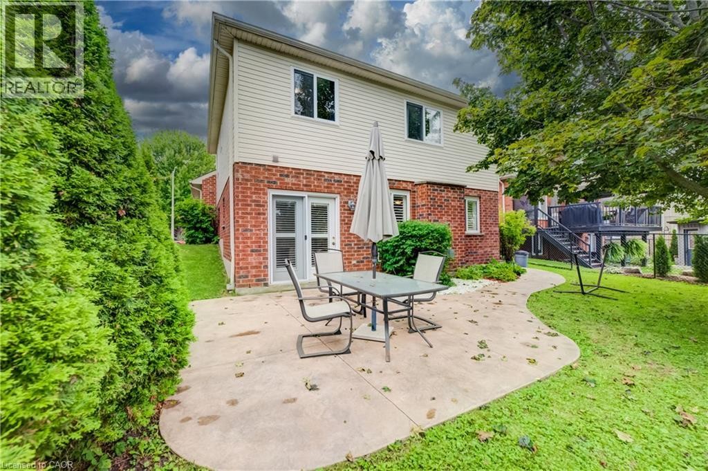 Brick and siding exterior featuring a concrete patio, mature trees, and privacy hedging - 245 Fern Crescent, Waterloo, ON