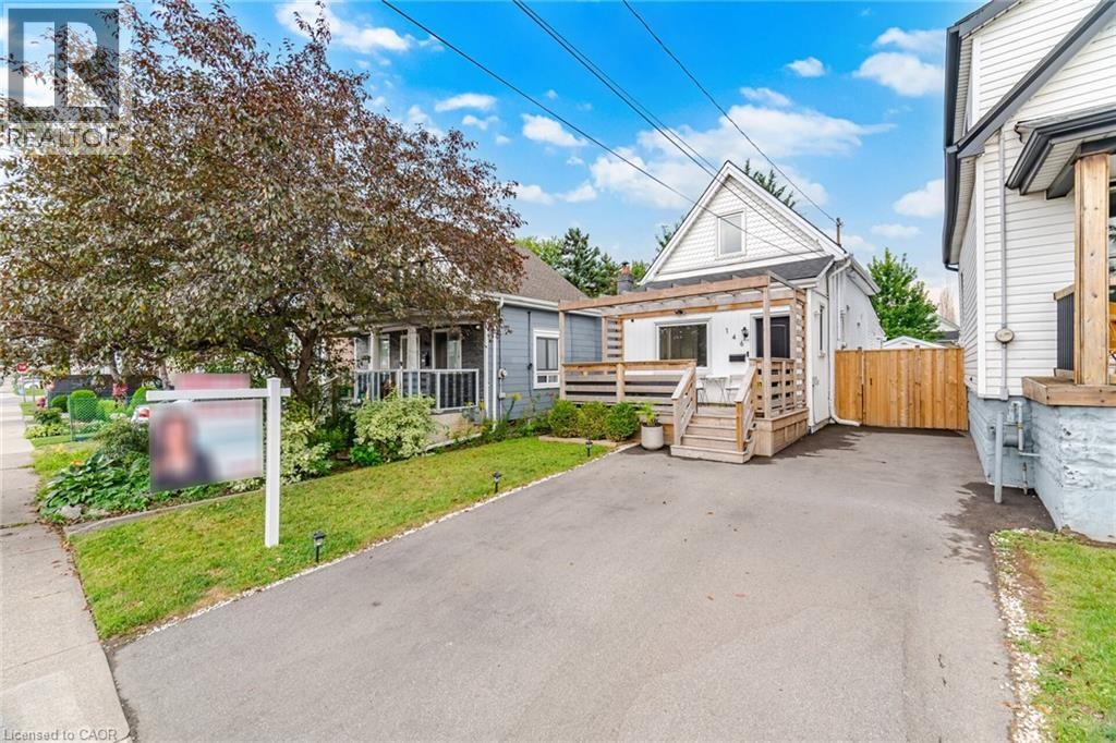 Paved driveway, wood deck with railing, gabled roofline, mature tree, and privacy fencing - 146 Campbell Avenue, Hamilton, ON