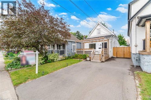 Paved driveway, wood deck with railing, gabled roofline, mature tree, and privacy fencing - 146 Campbell Avenue, Hamilton, ON 