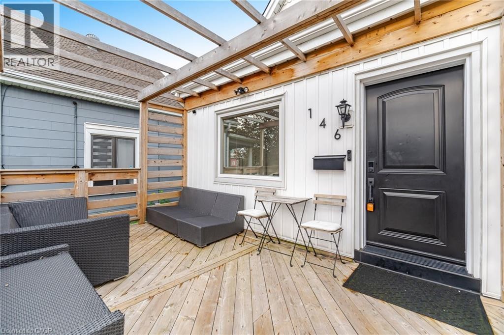 Wood-finish deck with a pergola structure, white exterior siding, and a black paneled entry door with an exterior wall light fixture - 146 Campbell Avenue, Hamilton, ON