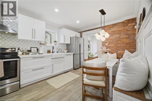 Modern kitchen featuring white cabinetry, stainless steel appliances, a white farmhouse sink, and wood-finish flooring - 146 Campbell Avenue, Hamilton, ON 