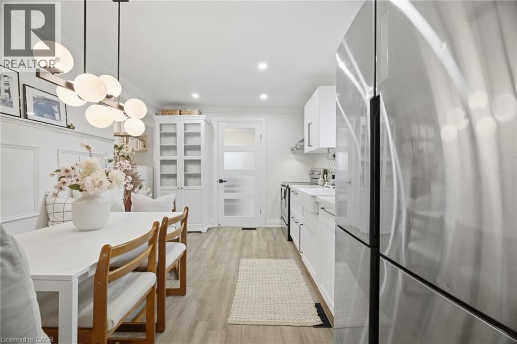 Stainless steel refrigerator, wood-finish flooring, recessed lighting, built-in cabinetry, and a modern globe chandelier - 146 Campbell Avenue, Hamilton, ON