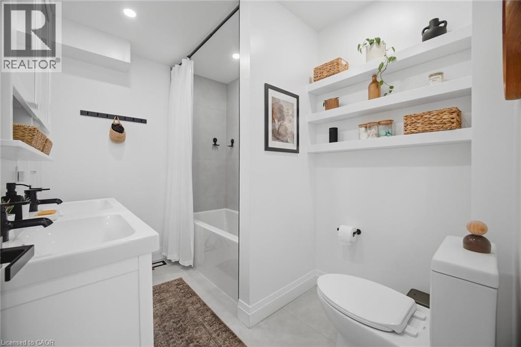 Dual-sink vanity with matte black fixtures, built-in shelving, recessed lighting, and a bathtub with a clear glass partition - 146 Campbell Avenue, Hamilton, ON