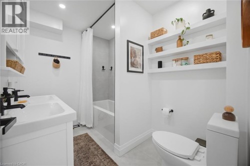 Dual-sink vanity with matte black fixtures, built-in shelving, recessed lighting, and a bathtub with a clear glass partition - 146 Campbell Avenue, Hamilton, ON 