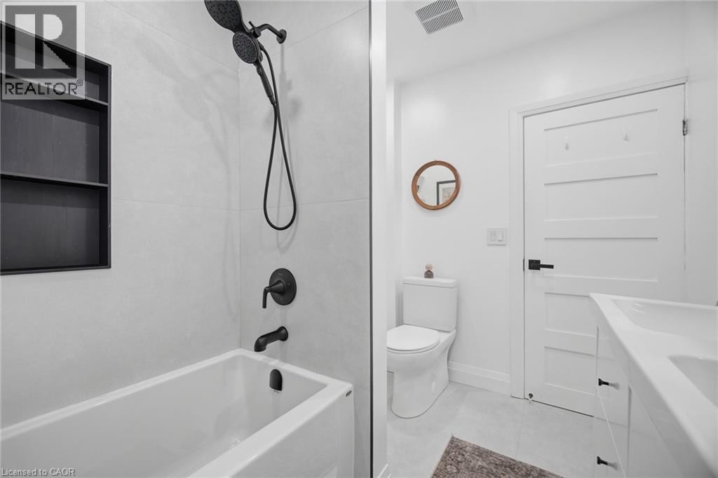 Bathtub with matte black fixtures, an integrated shower niche, and white subway-style wall tiling - 146 Campbell Avenue, Hamilton, ON