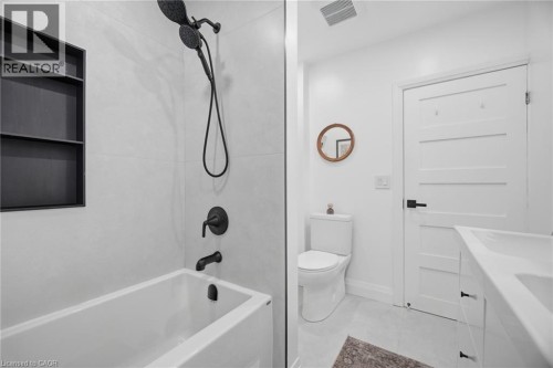 Bathtub with matte black fixtures, an integrated shower niche, and white subway-style wall tiling - 146 Campbell Avenue, Hamilton, ON 