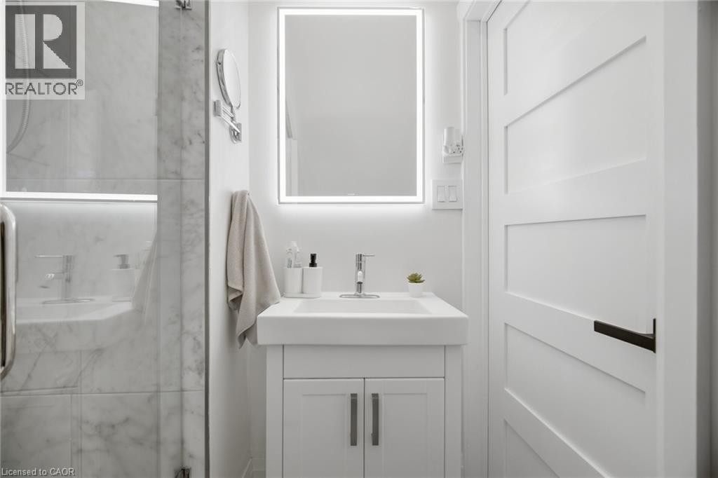 White shaker-style vanity with integrated sink, chrome faucet, and rectangular LED-lit mirror - 146 Campbell Avenue, Hamilton, ON